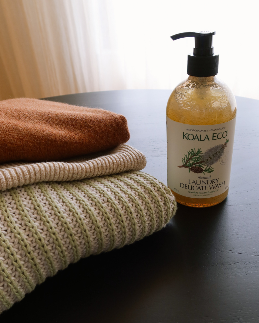 How To Care For ROWIE The Label Knitwear and Delicate Clothing. A bottle of Koala Eco Natural Laundry Delicate Wash sits on a table with ROWIE Autumn/Winter '24 Knitwear.