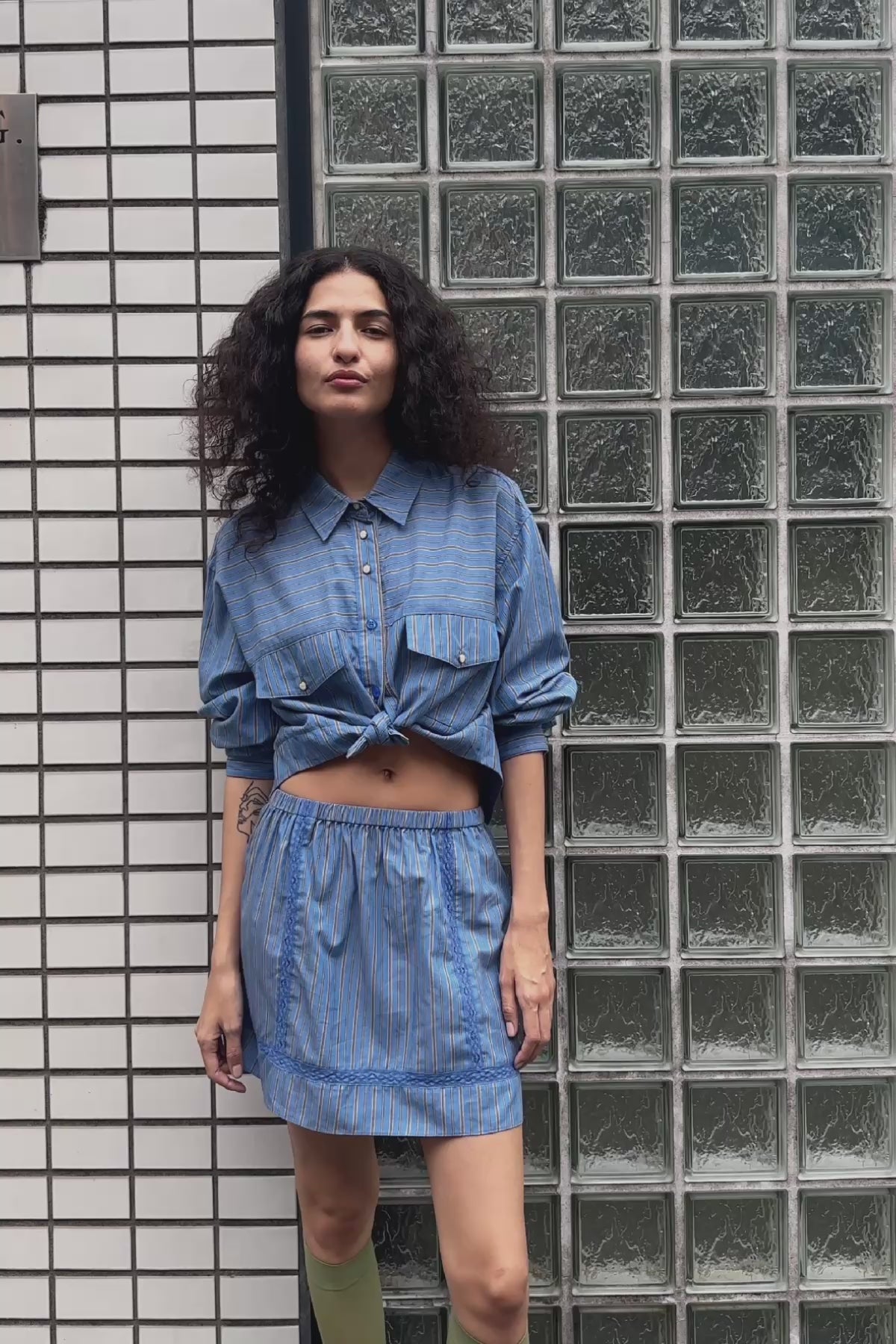 Video of model wearing a Suri Lace Mini Skirt in Lagoon, styled with the Cole Stripe Crop Shirt in Lagoon by ROWIE the Label, filmed on a Tokyo street.
