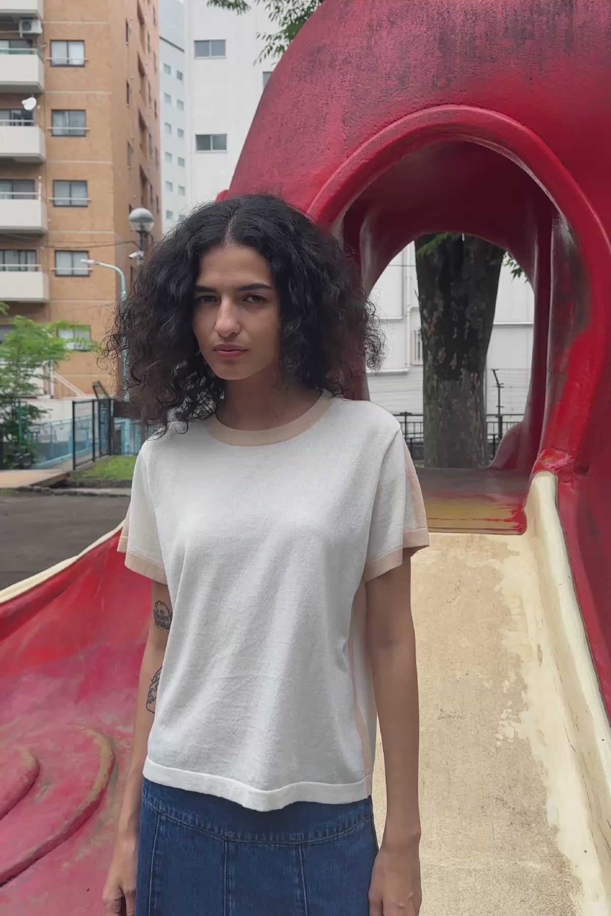 Video of model wearing a Vashti Denim Midi Skirt in Classic Denim, styled with the Rania Contrast Knit Tee in Oat Milk by ROWIE the Label, filmed at a playground in Tokyo.
