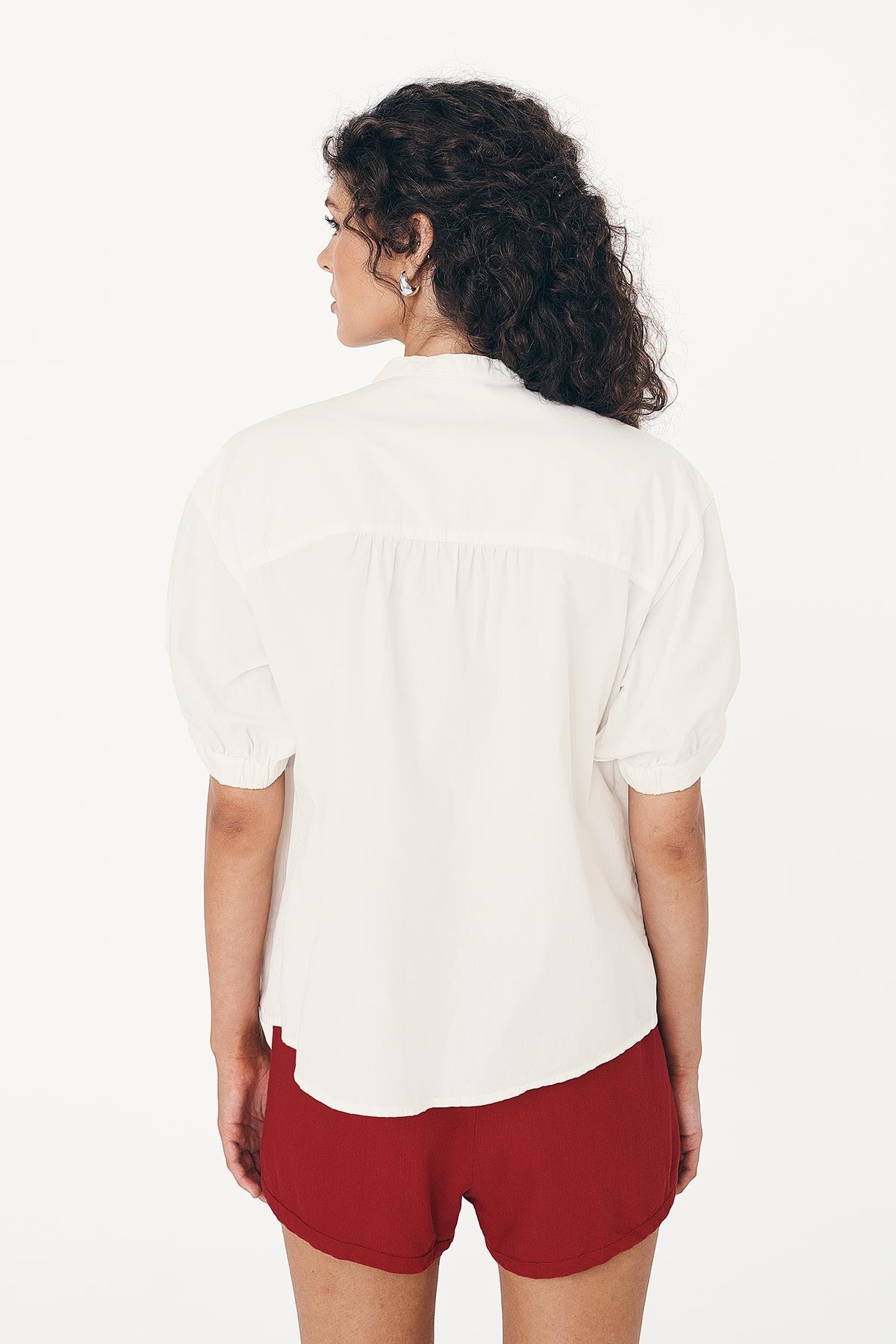 Model wearing a white Cora Spring Blouse and red Simone Linen Shorts on a white background