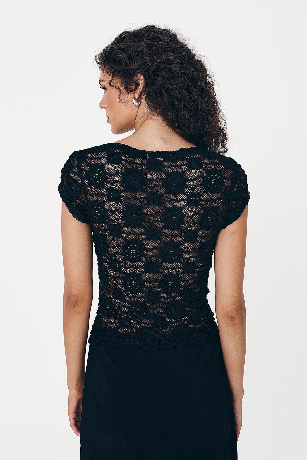 Model wears a black lace top, with woven floral detail and paired with a black silk skirt against a white background