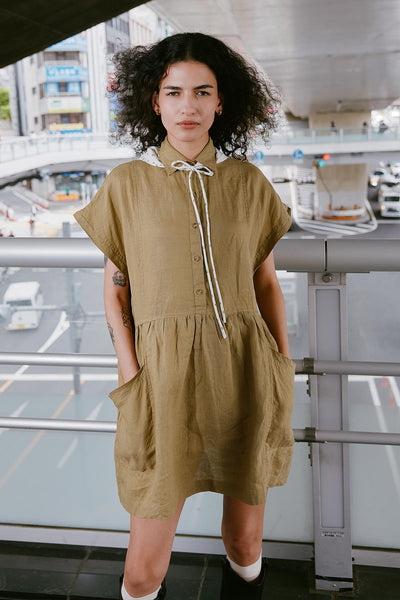 Model wearing a Gina Linen Mini Dress in Dusty Olive by ROWIE the Label, styled with a Frannie Silk Belt Scarf in Vanilla Spot tied around her neck, lifestyle shot in Tokyo.