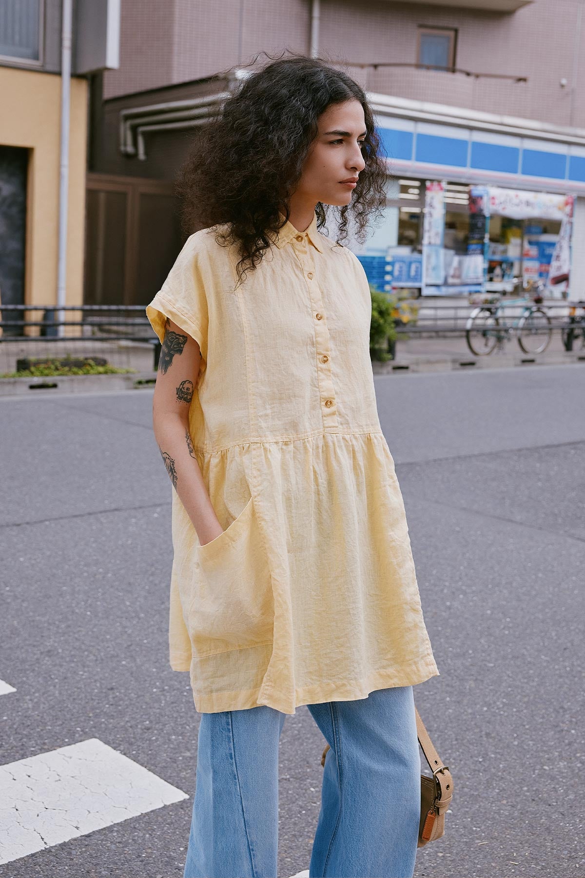 Woman walking through the street in Japan wearing a Gina Linen Mini Dress and Percy Curve Seam Jeans in Washed Denim by ROWIE the Label