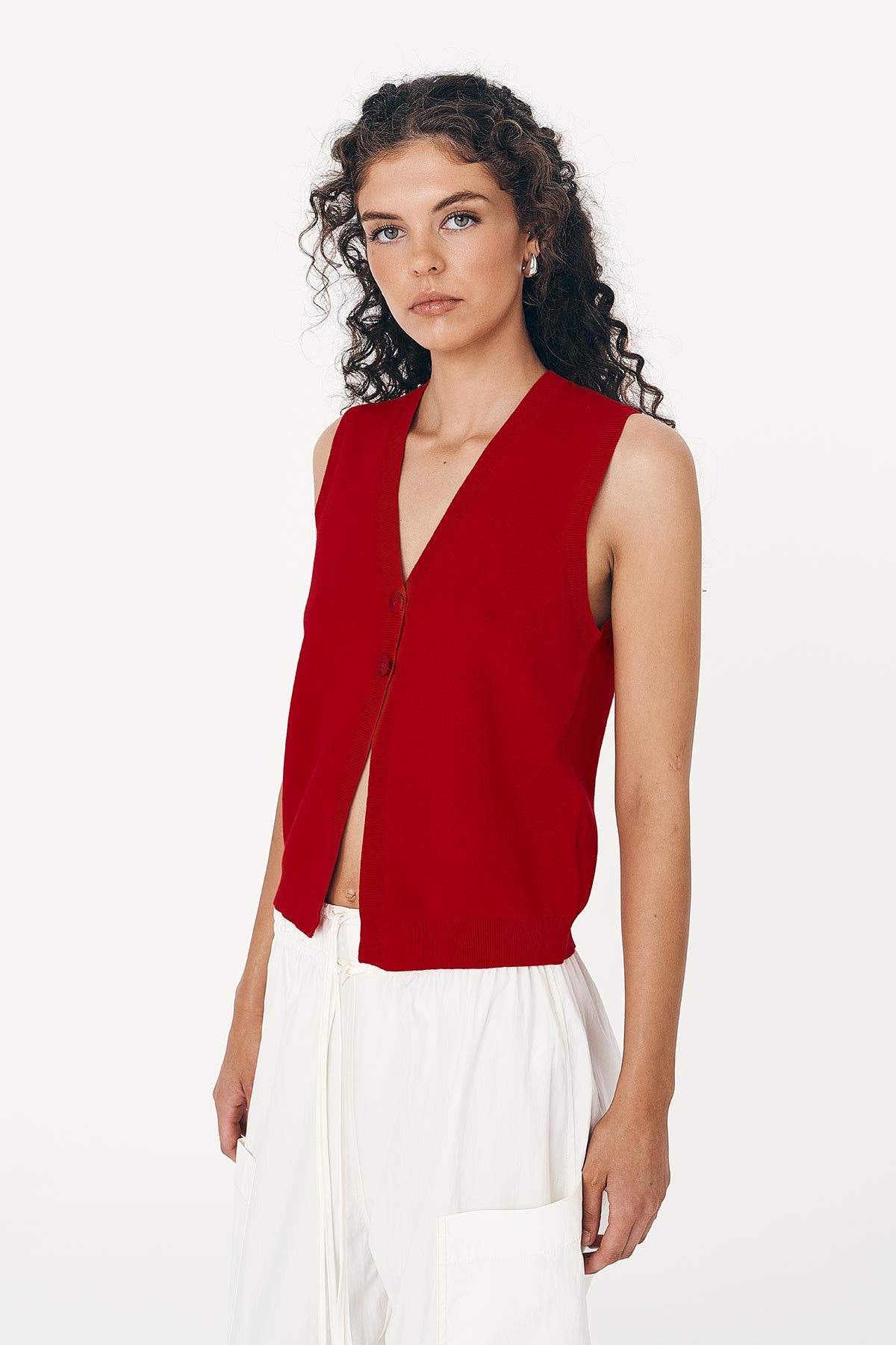 Model wears a red sleeveless knit top and white cargo pants on a white background