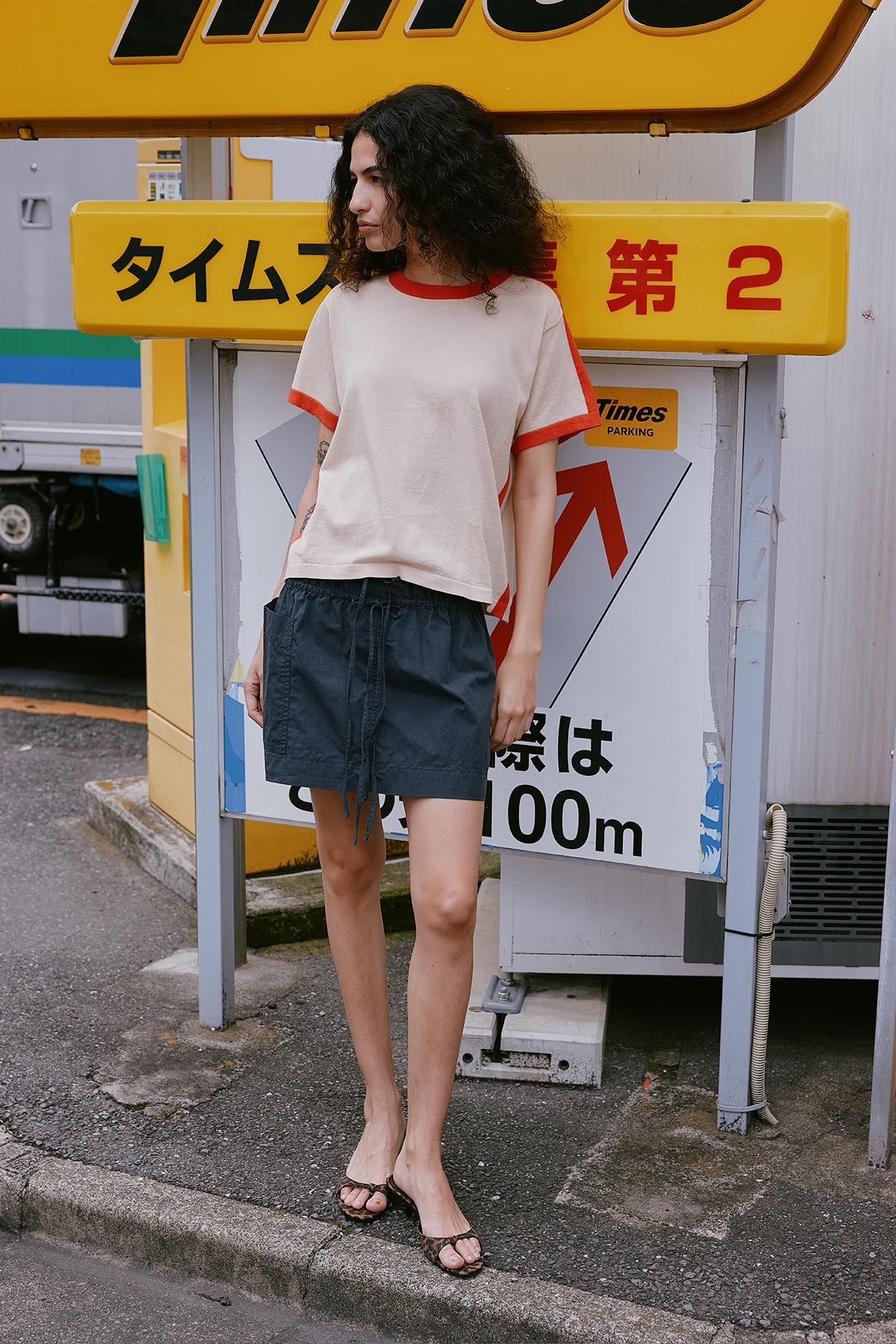 Model stands in front of a sign in Japan wearing ROWIE The Label Rania Contrast Cotton Knit Tee Shirt paired with the Jessica Cargo Mini Skirt in Washed Ink Black