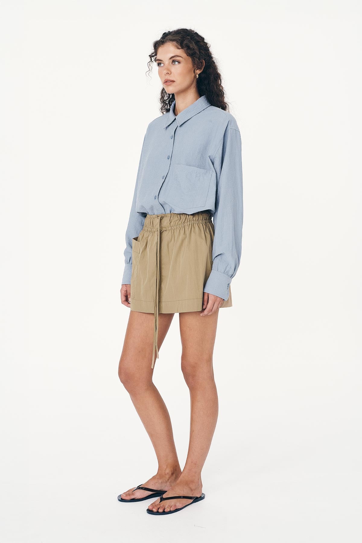 Angled side studio view of model wearing a Jessica Cargo Mini Skirt in Washed Khaki, styled with the Ramona Silk Long Sleeve Shirt in Periwinkle Blue by ROWIE the Label.