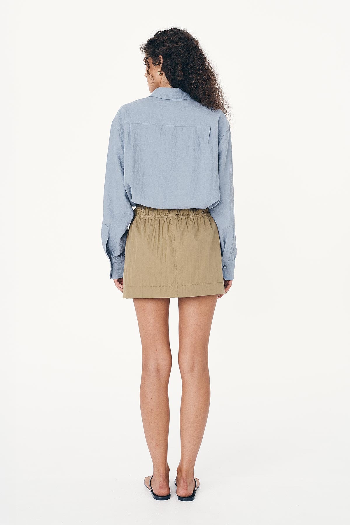 Back studio view of model wearing a Jessica Cargo Mini Skirt in Washed Khaki, styled with the Ramona Silk Long Sleeve Shirt in Periwinkle by ROWIE the Label.