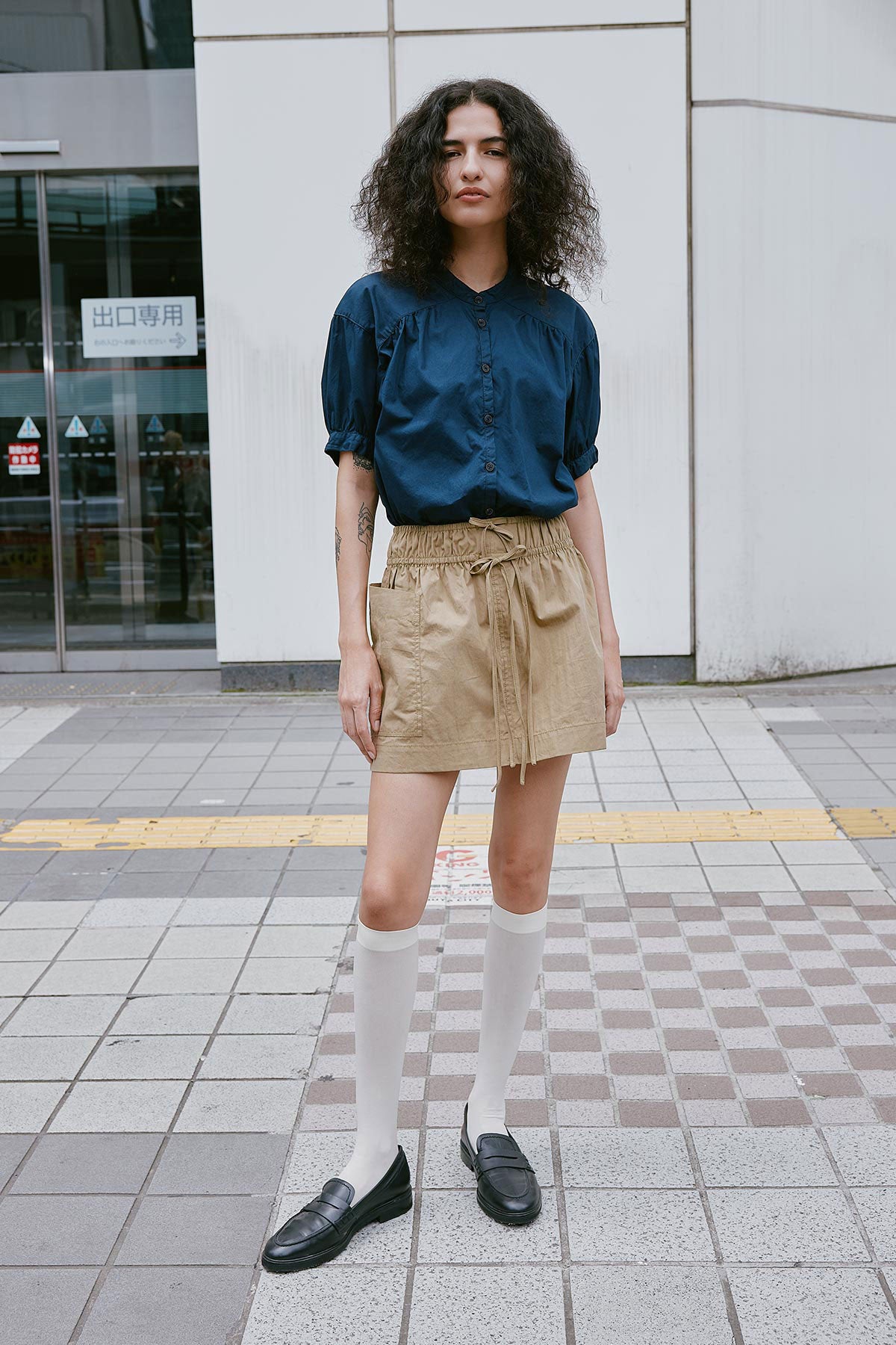 Model wearing a Jessica Cargo Mini Skirt in Washed Khaki, styled with the Cora Spring Blouse in Ink Cotton by ROWIE the Label, lifestyle shot on a Tokyo street.