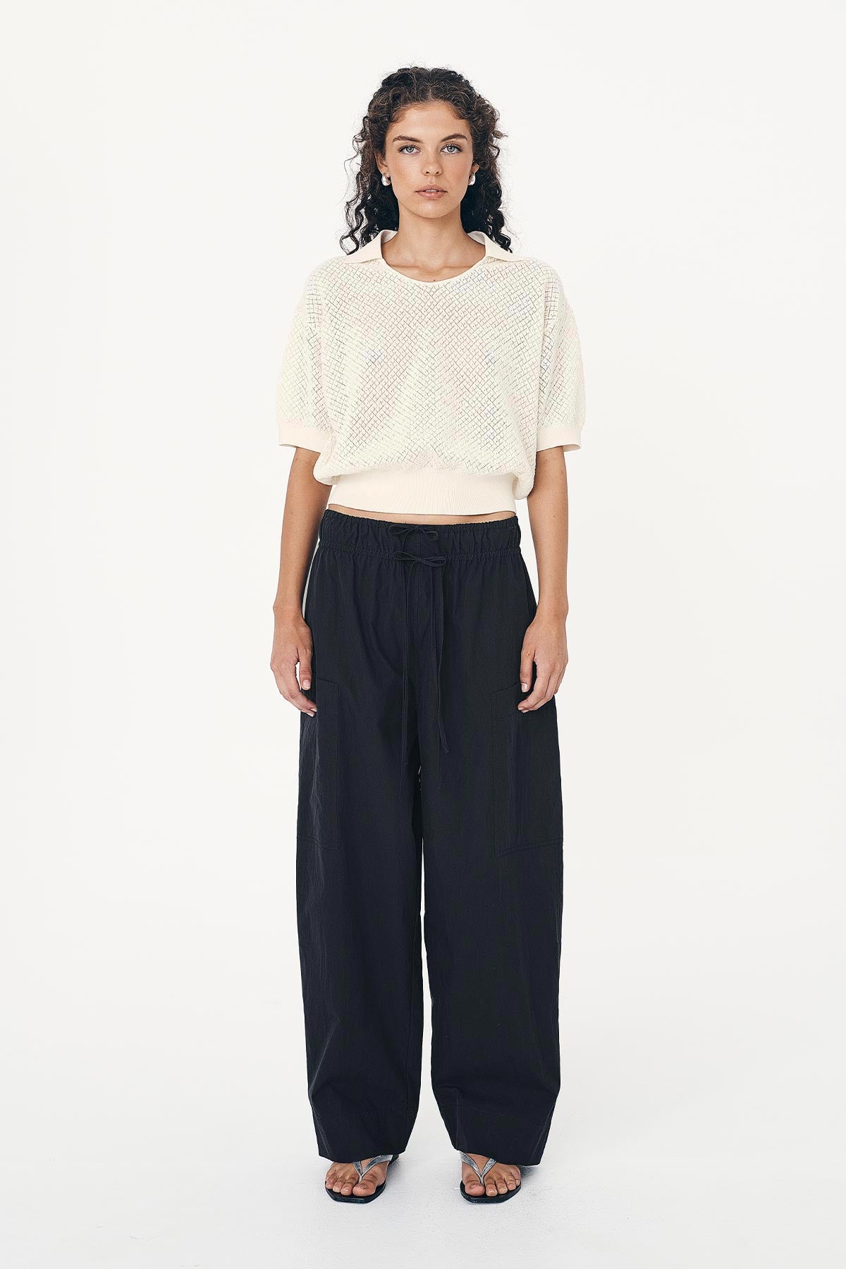 Woman wears Jessica Cargo Pants in Black, paired with a Loretta Pointelle Knit Top, in creme against a white background