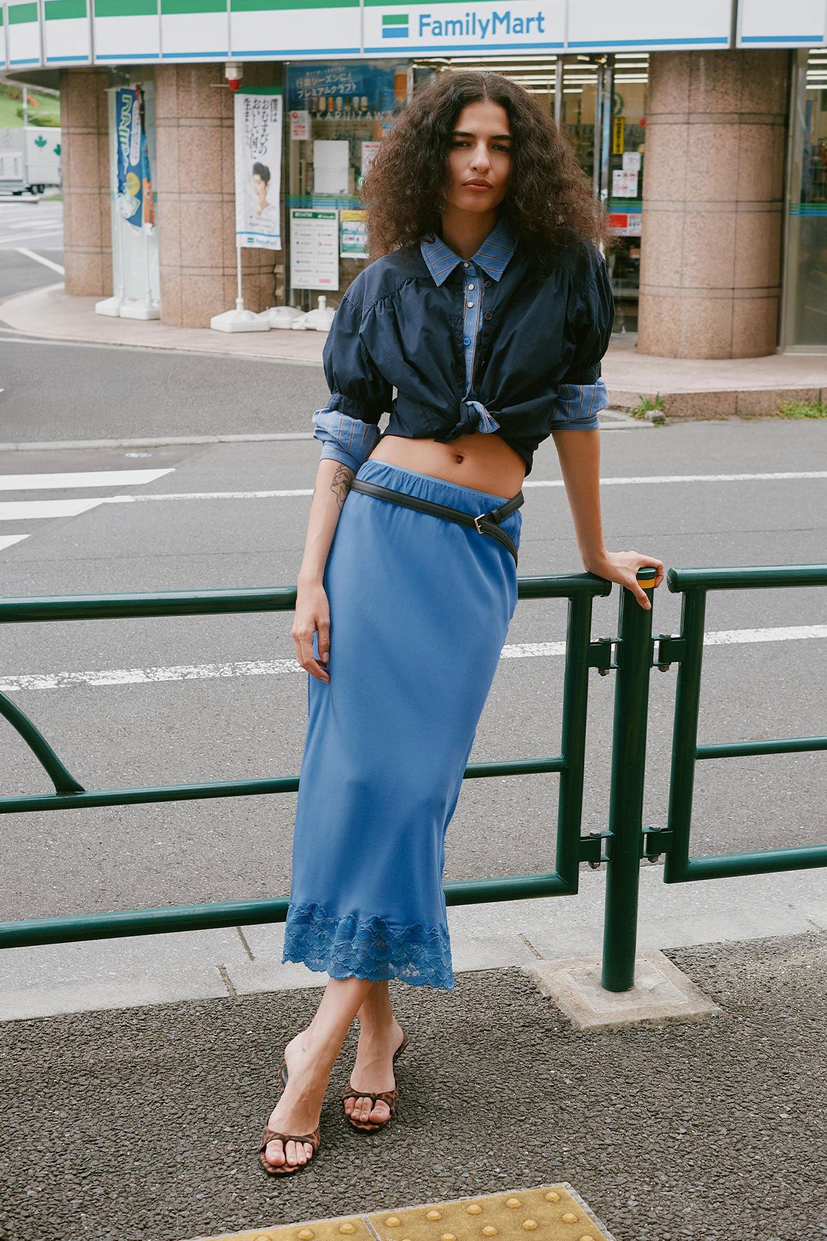 Model wearing a Marina Silk Midi Skirt in Cornflower, styled with a Ramona Silk Long Sleeve Shirt in Periwinkle layered under a Cora Spring Blouse in Ink Cotton by ROWIE the Label, lifestyle shot on a Tokyo street.