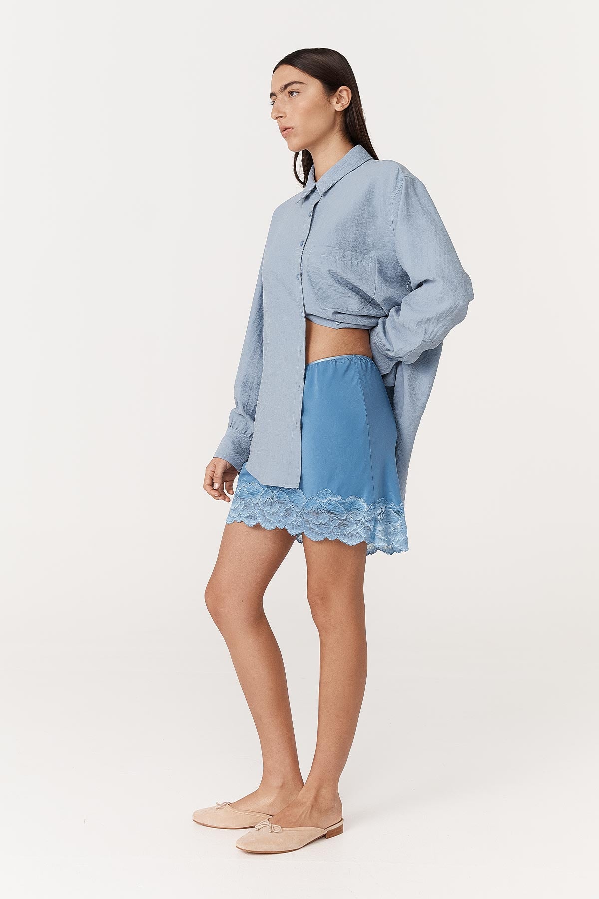 Angled side studio view of model wearing a Marina Silk Mini Skirt in Cornflower, styled with the Ramona Silk Long Sleeve Shirt in Periwinkle by ROWIE the Label.