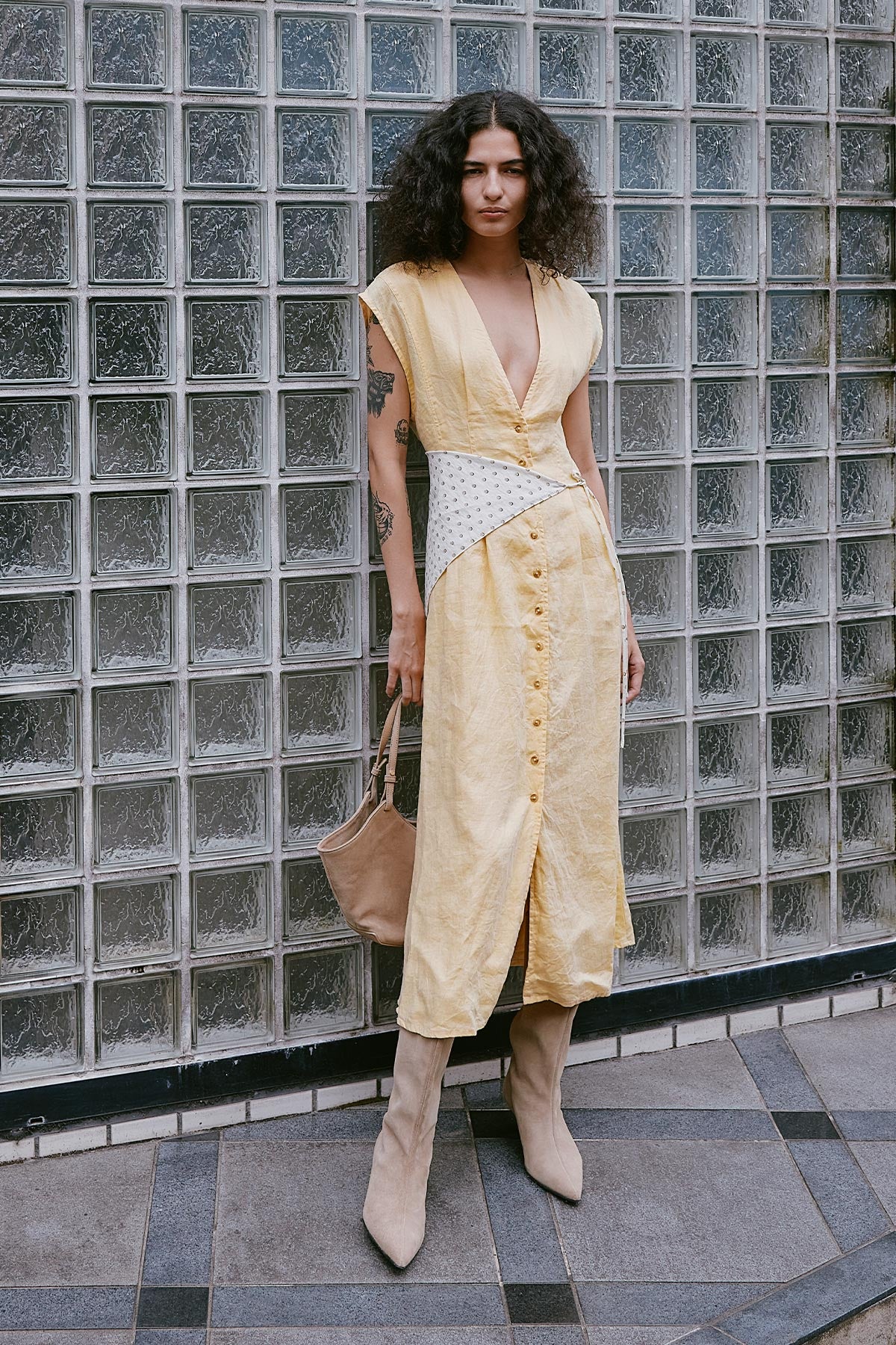 Model stands in a ROWIE The Label Mira Linen Dress, with deep neckline and button up dress, paired with the Frannie Silk Scarf and beige suede knee-high boots