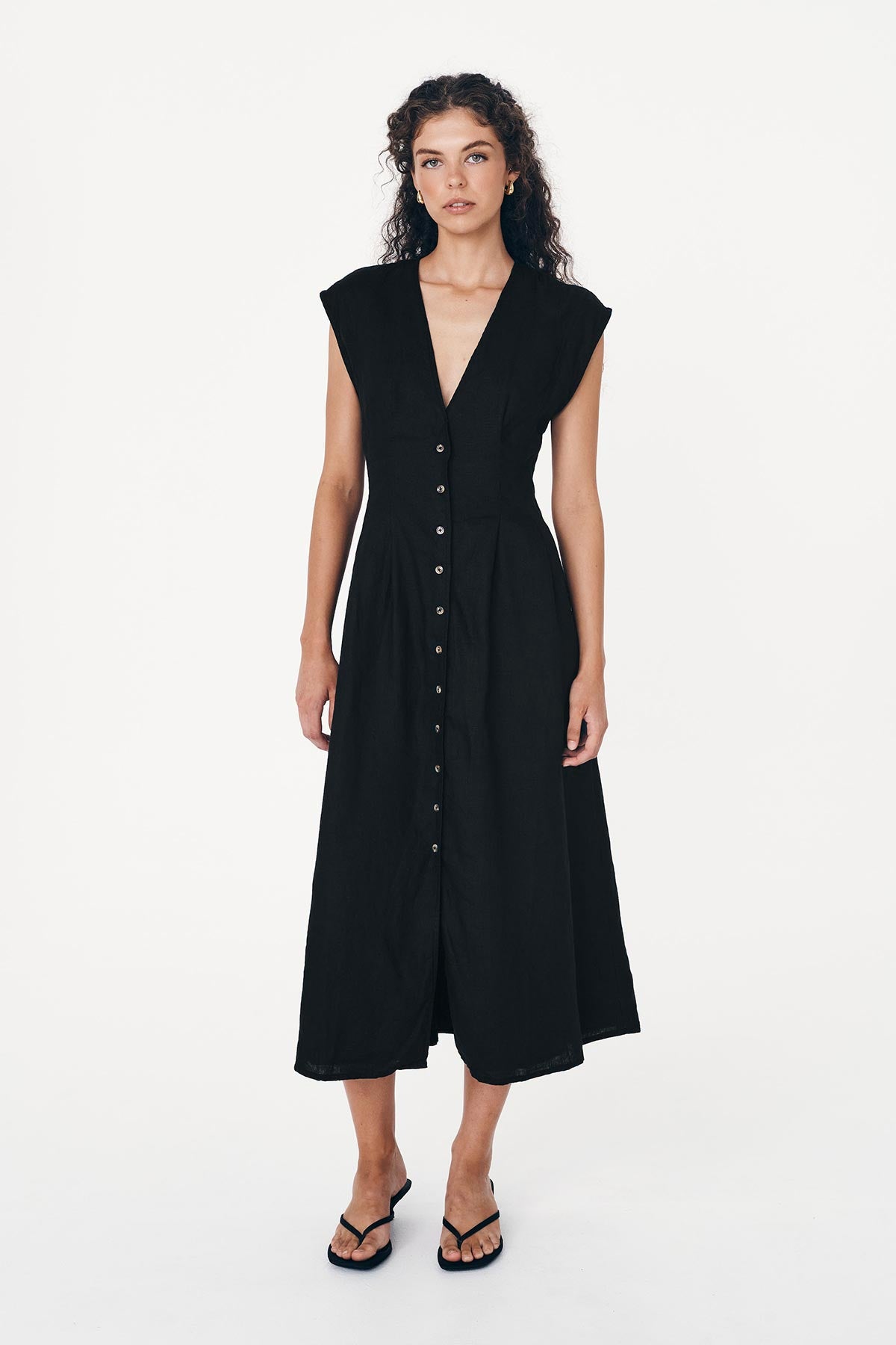 Model wears a Mira Linen Midi Dress in Black. A sleeveless dress featuring a deep neckline, button-through front, and tie-back waist by ROWIE The Label