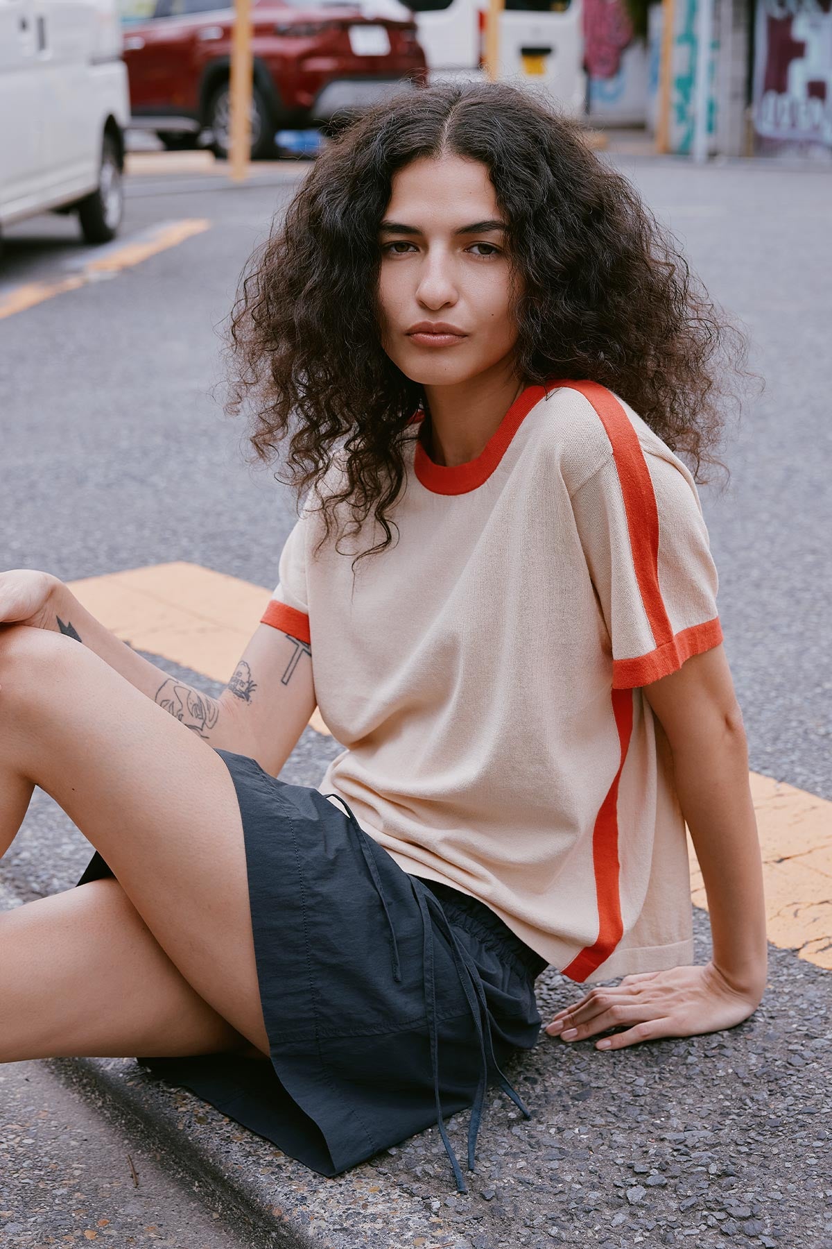 Woman sitting on a street curb in Japan wearing a beige and red Contrast Tee Shirt by ROWIE The Label, paired with the Jessica Cargo Mini Skirt in Ink Black