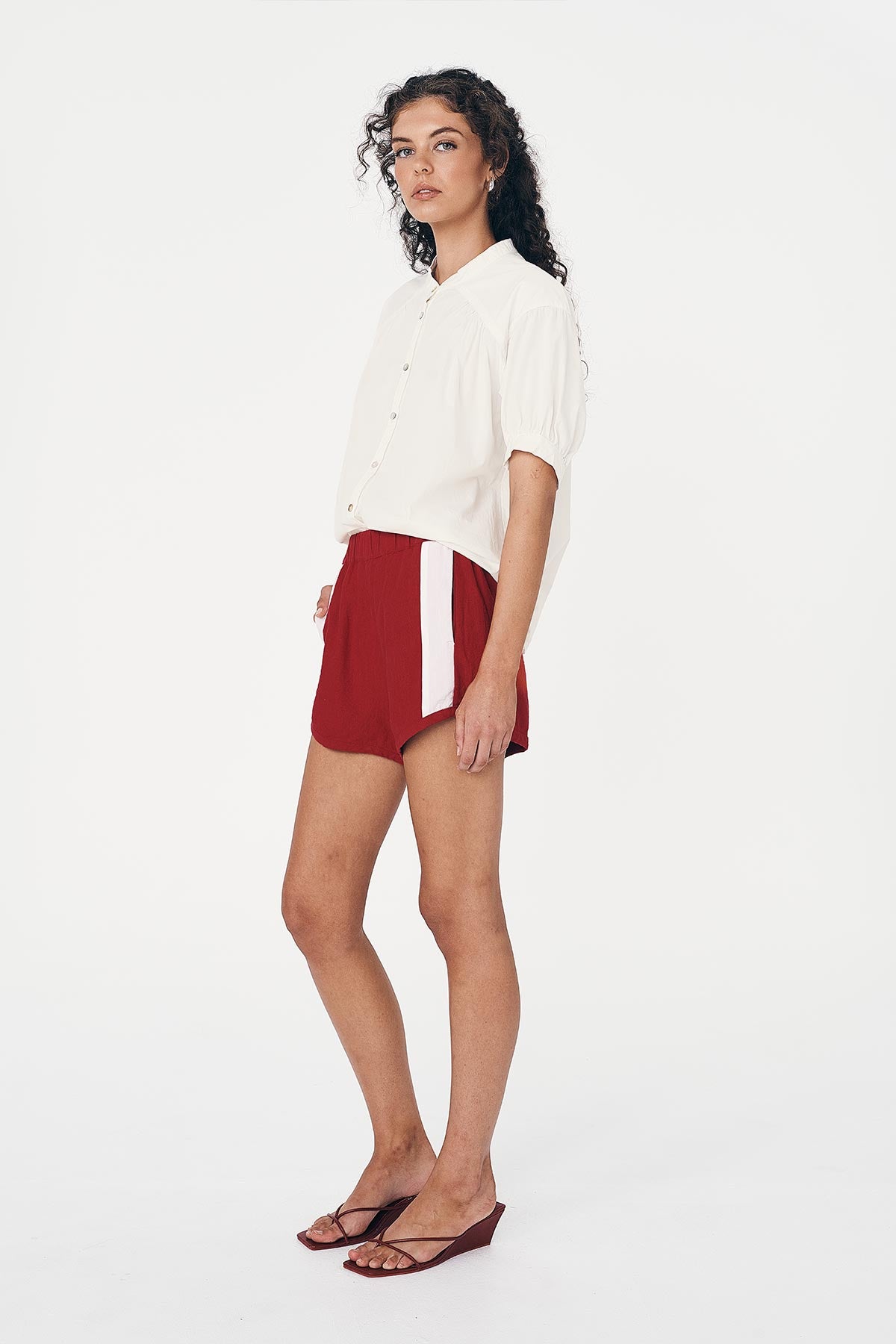 Woman wearing a white Cora Spring Blouse and red Simone Linen Shorts by Australian brand ROWIE The Label