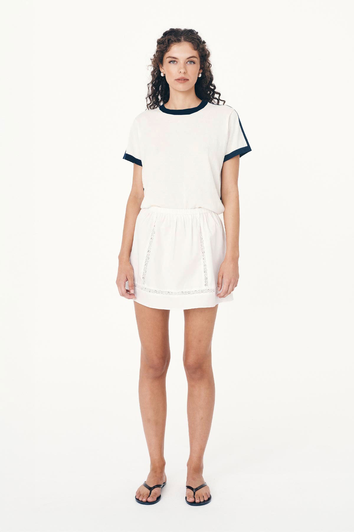 Full-body studio view of model wearing a Suri Lace Mini Skirt in Bone, styled with the Rania Contrast Knit Tee in Ink by ROWIE the Label.