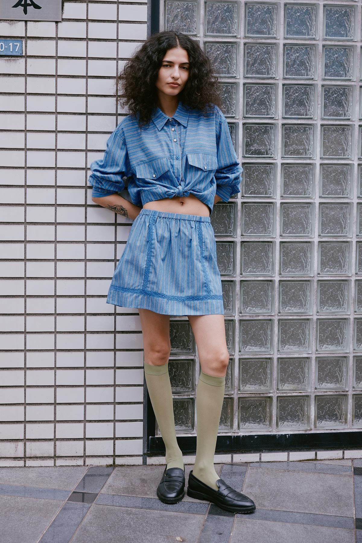 Model wearing a Suri Lace Mini Skirt in Lagoon, styled with the Cole Stripe Crop Shirt in Lagoon by ROWIE the Label, lifestyle shot on a Tokyo street.