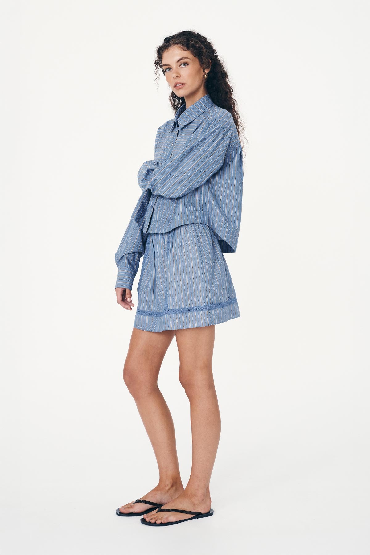 Angled side studio view of model wearing a Suri Lace Mini Skirt in Lagoon, styled with the Cole Stripe Crop Shirt in Lagoon by ROWIE the Label.
