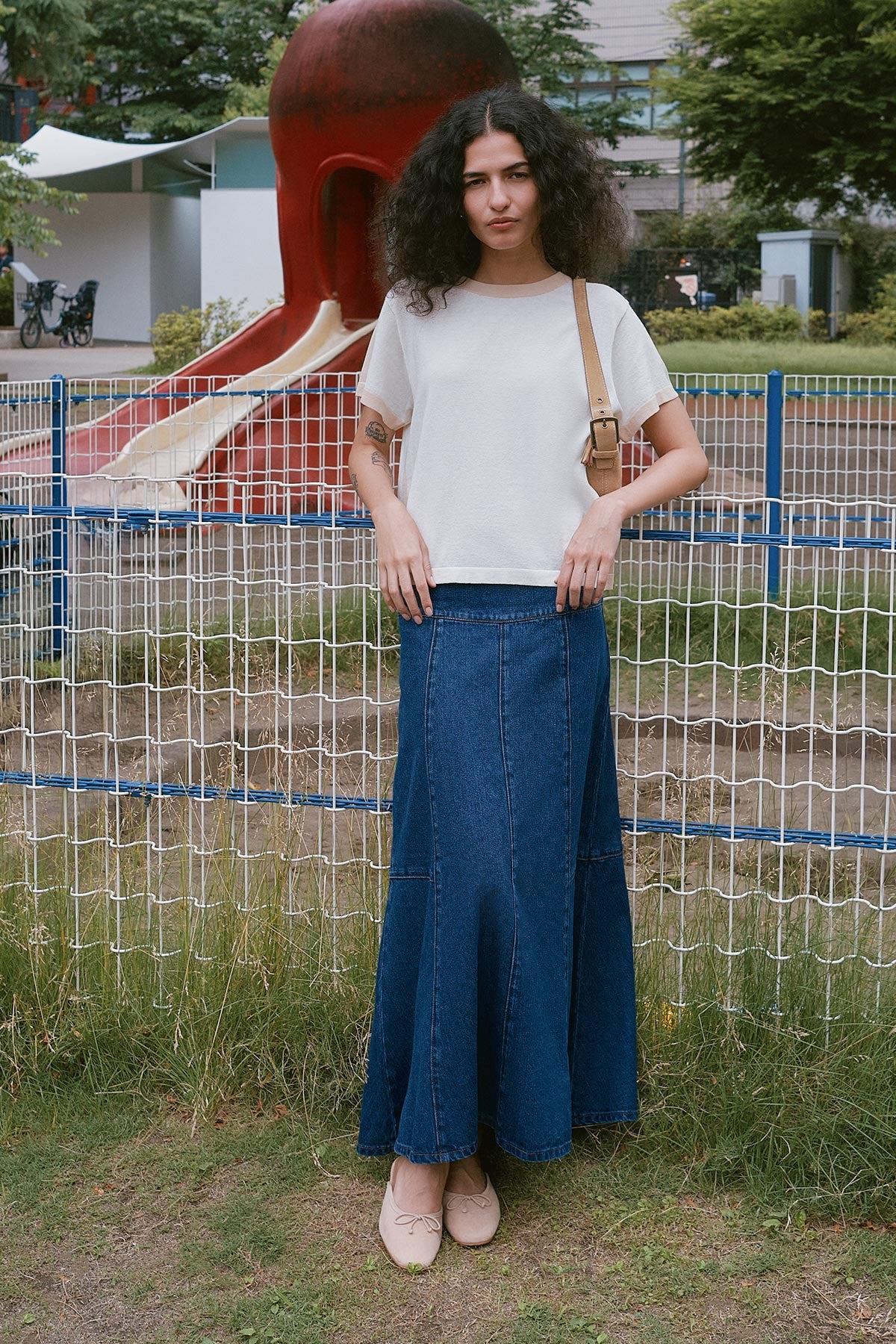 Model wearing a Vashti Denim Midi Skirt in Classic Denim, styled with the Rania Contrast Knit Tee in Oat Milk by ROWIE the Label, lifestyle shot at a playground in Tokyo.